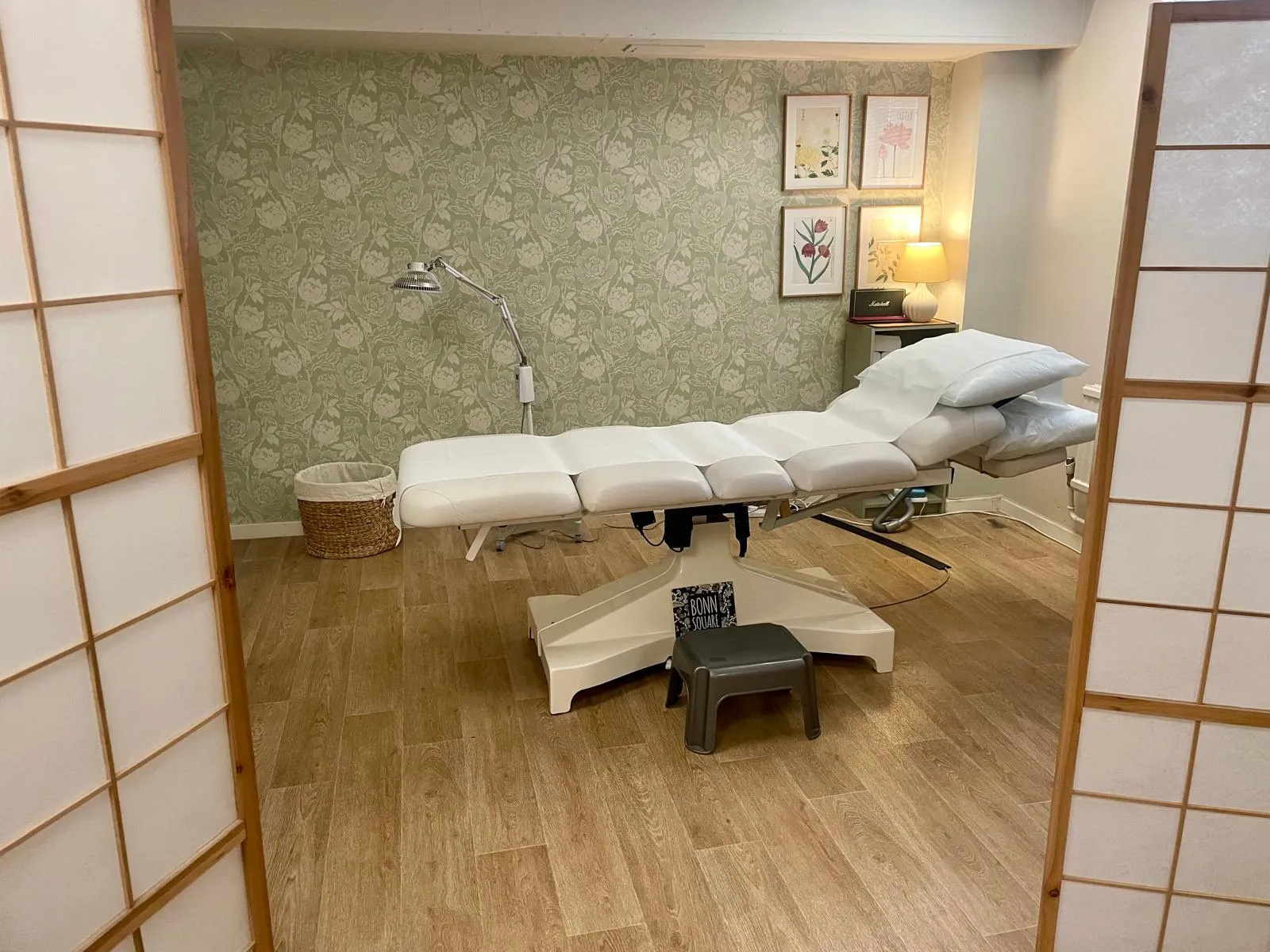 Treatment room at Bonn Square Therapy Room, with a treatment couch, a green patterned wall and privacy screens